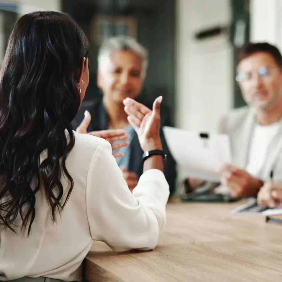 Persona gesticulando en una reunión de negocios con dos colegas.