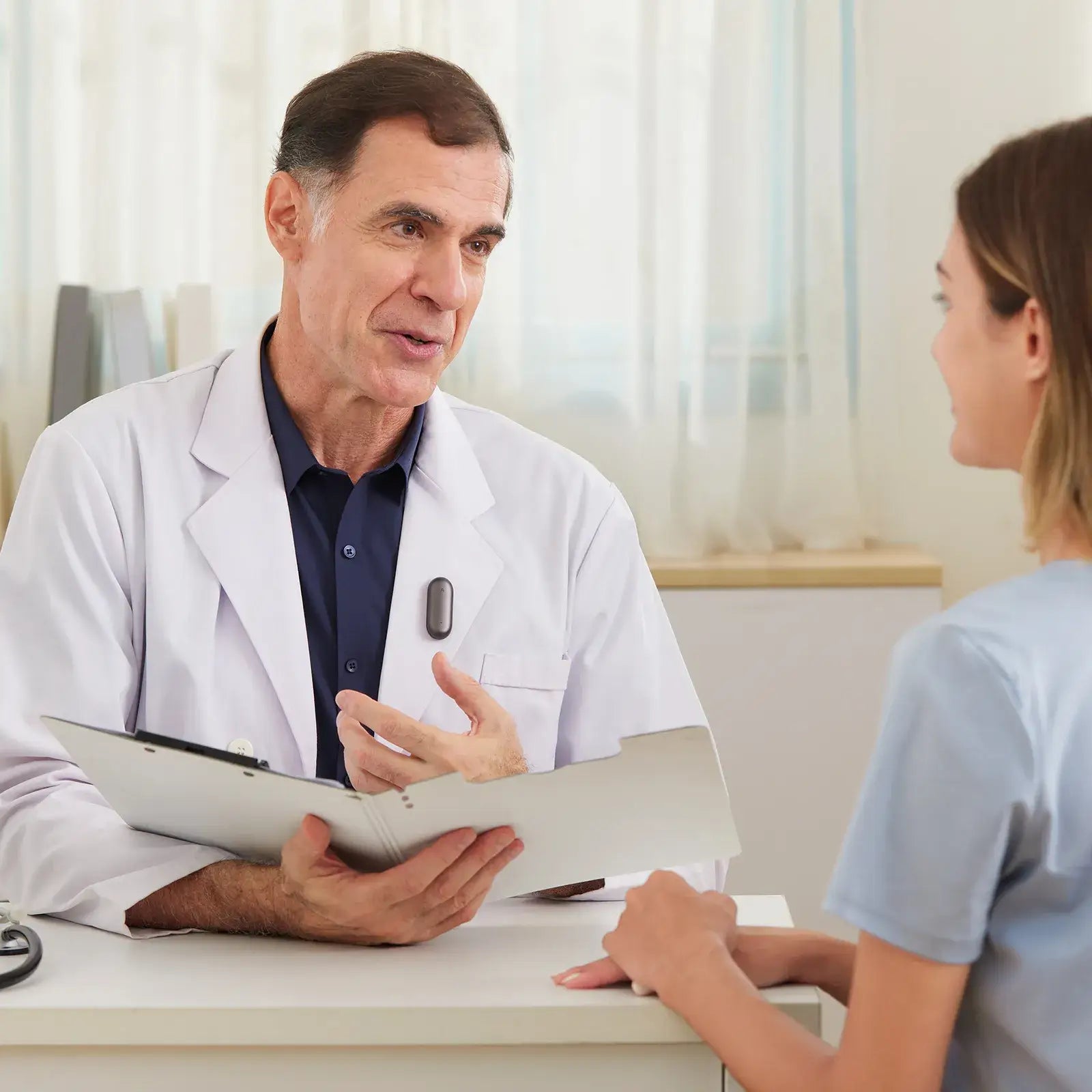 Doctor con Plaud NotePin negro en su bata, hablando con una paciente en una consulta.