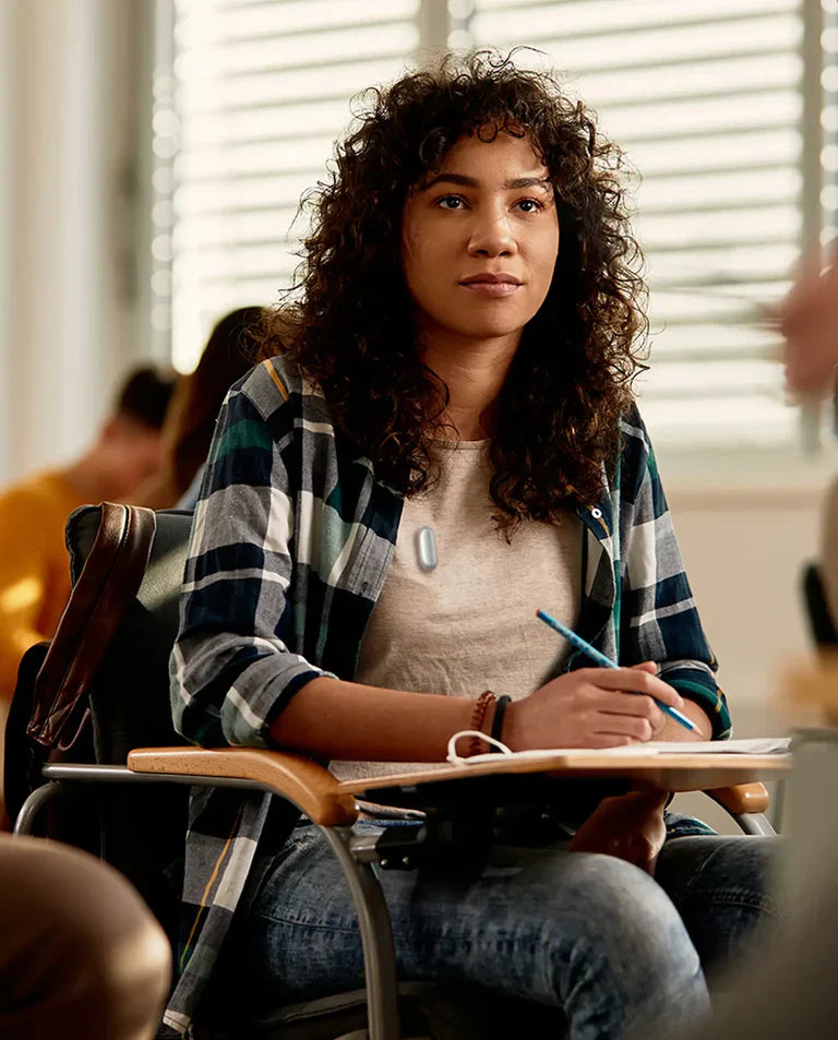 Joven estudiante con Plaud NotePin plateado en el aula, atenta y tomando notas.