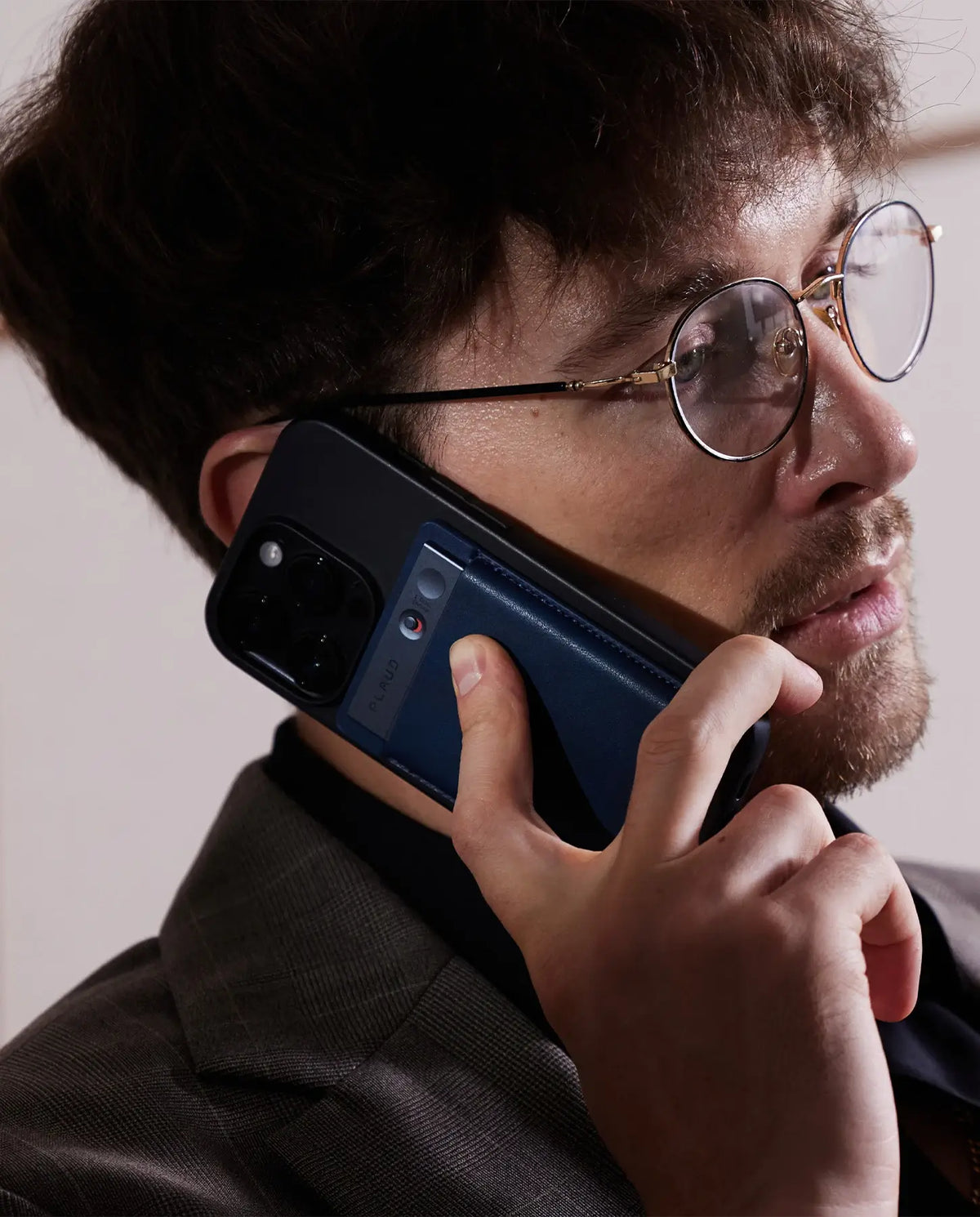 Hombre con gafas hablando por teléfono, con un Plaud Note azul acoplado a la parte trasera de su móvil.