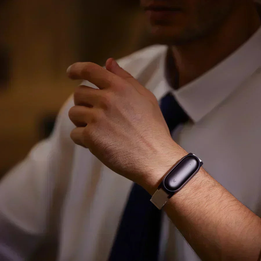 Primer plano de una persona con un Plaud NotePin oscuro en una pulsera clara, camisa blanca y corbata oscura.