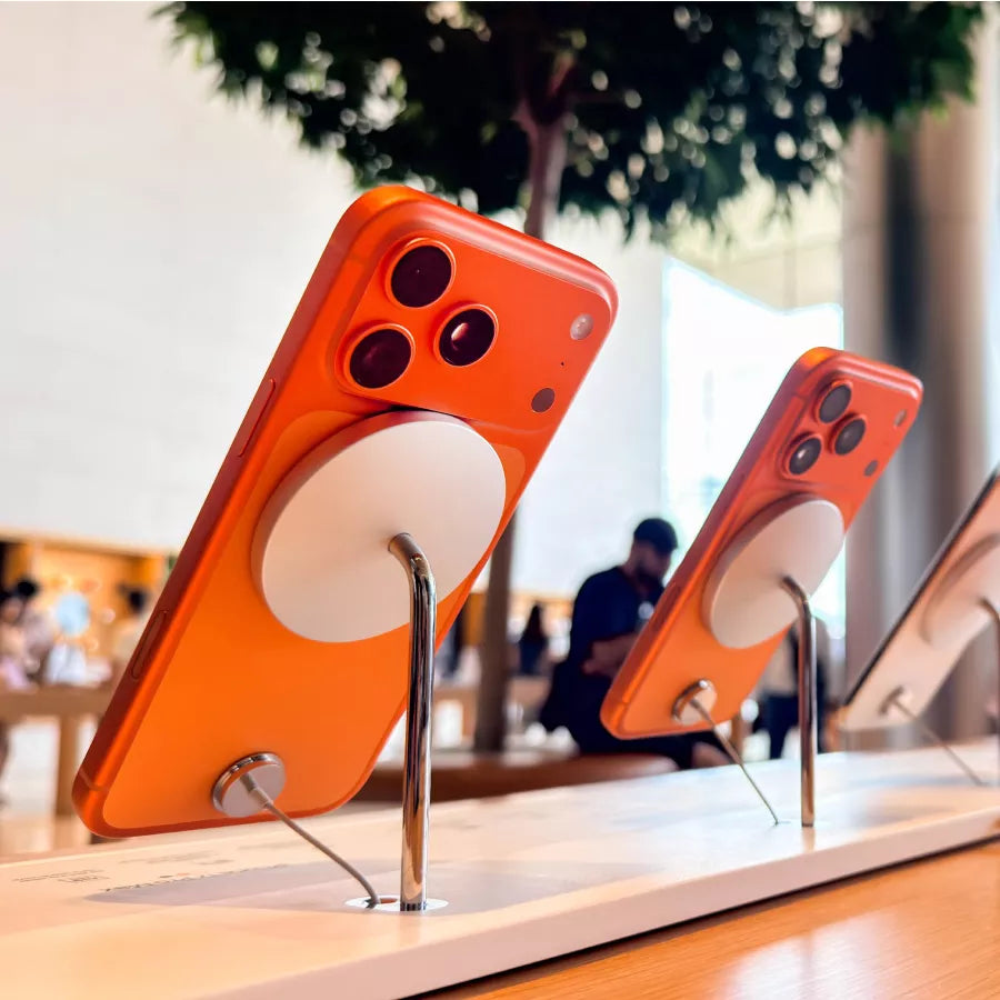 Teléfonos inteligentes naranjas en exhibición en una tienda. Se ven las cámaras traseras y un accesorio magnético circular.
