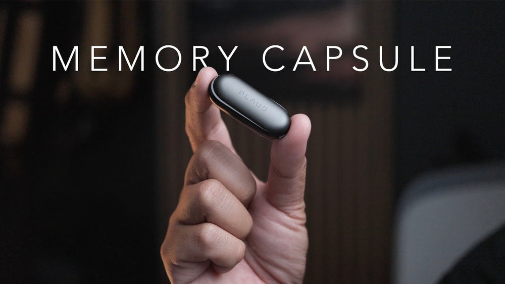 Mano sosteniendo un Plaud NotePin negro entre dos dedos, con el texto 'MEMORY CAPSULE' de fondo.