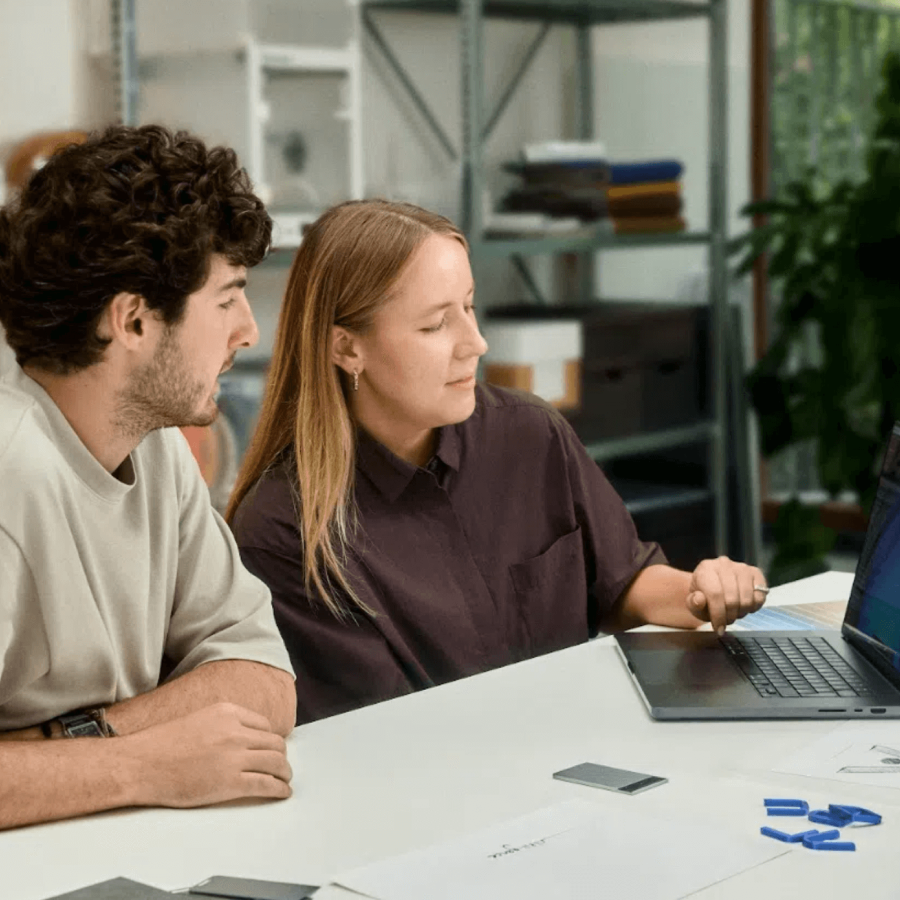 Dos personas colaboran mirando una laptop, con un Plaud Note Pro negro sobre la mesa.