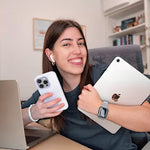 Mujer sonriente con iPhone blanco, iPad plateado, AirPods y smartwatch en un entorno de oficina.