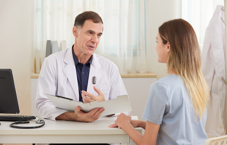 Doctor con Plaud NotePin S negro en la bata, hablando con una paciente en una consulta médica.