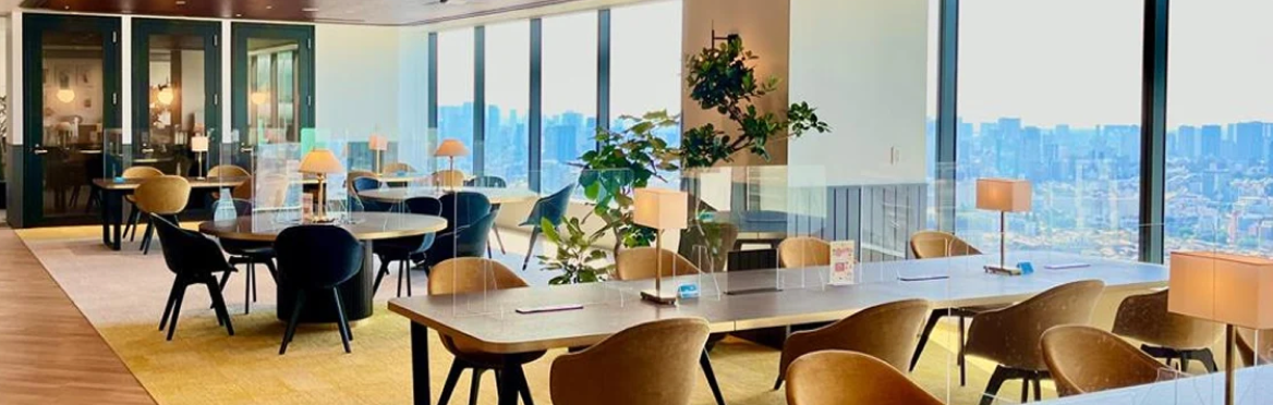 Espacio de oficina moderno con grandes ventanales, mesas y sillas, y vista a la ciudad.
