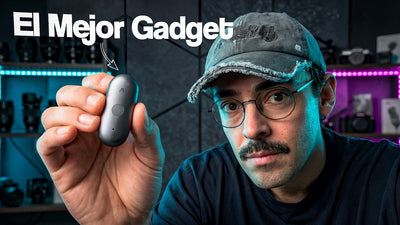 Hombre con gafas y gorra sostiene un Plaud NotePin gris oscuro, con estantes iluminados al fondo.