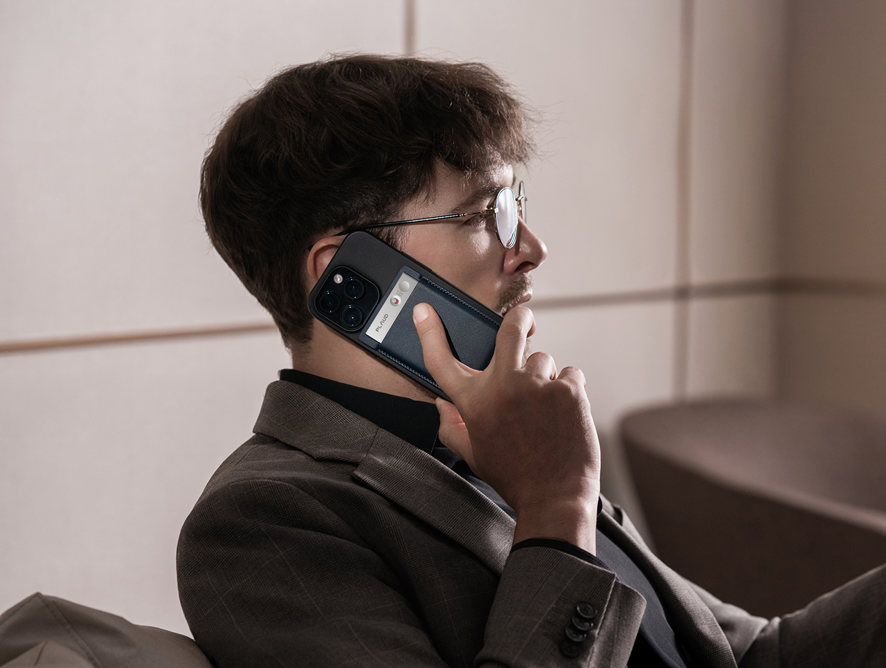 Hombre en una llamada con un Plaud Note negro acoplado a su teléfono, grabando la conversación.
