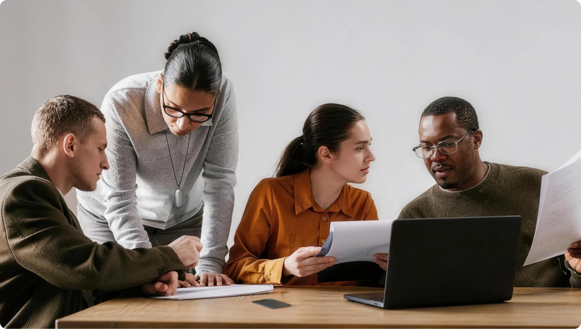 Cuatro personas colaborando en una mesa, revisando documentos y un portátil.
