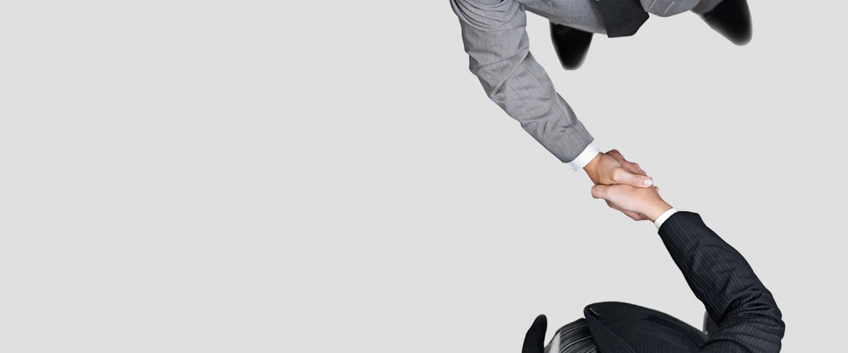 Vista superior de dos personas de negocios dándose la mano, una con traje gris y otra oscuro.