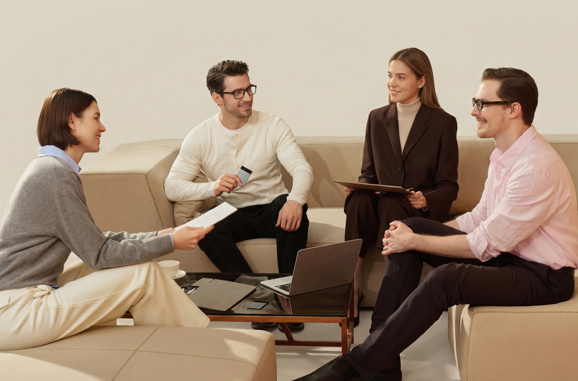 Cuatro profesionales conversan sentados en un sofá beige; un hombre sostiene un Plaud Note Pro plateado mientras colaboran con una laptop y documentos.