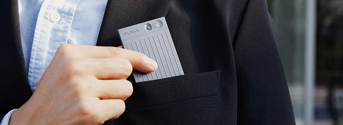 Mano metiendo un Plaud Note gris en el bolsillo de una chaqueta de traje.