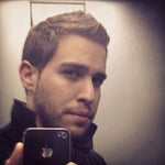 Hombre joven con barba tomando una selfie en un espejo con un iPhone negro.