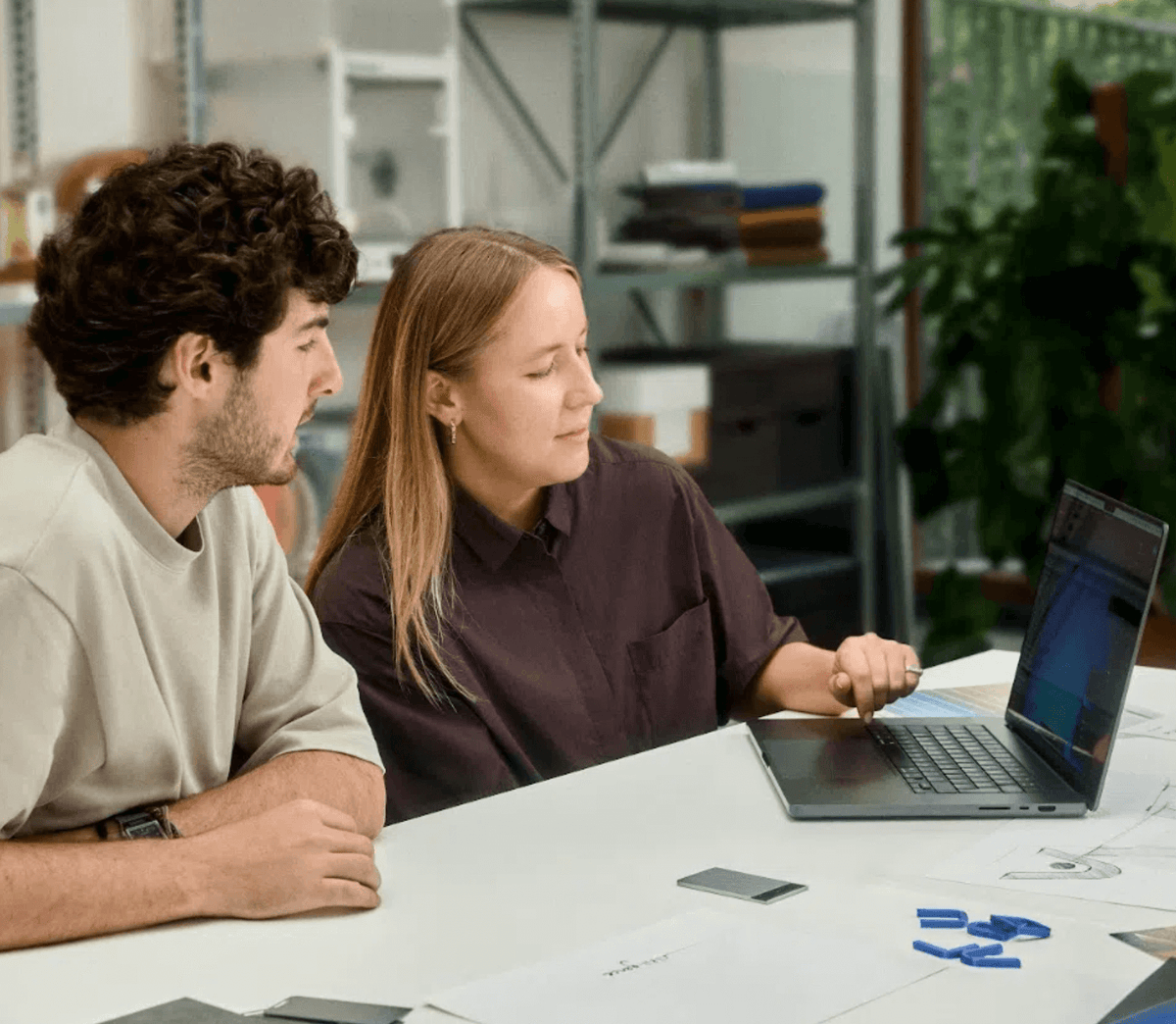 Dos personas colaboran en una laptop, con un Plaud Note Pro negro en la mesa, en un entorno de oficina.